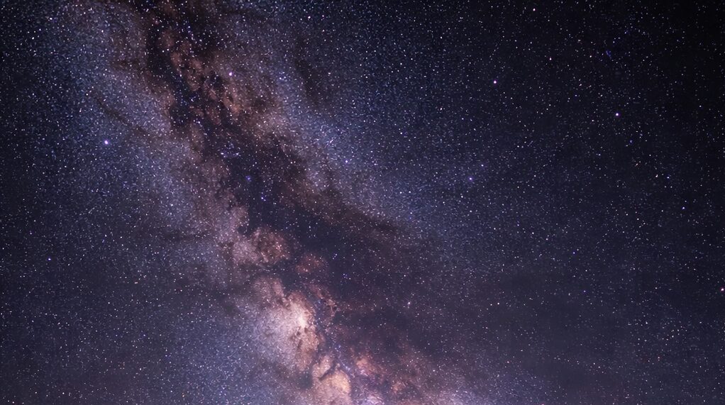 Fotograf stojí so statívom pod hviezdnou oblohou pri fotografovaní Mliečnej dráhy