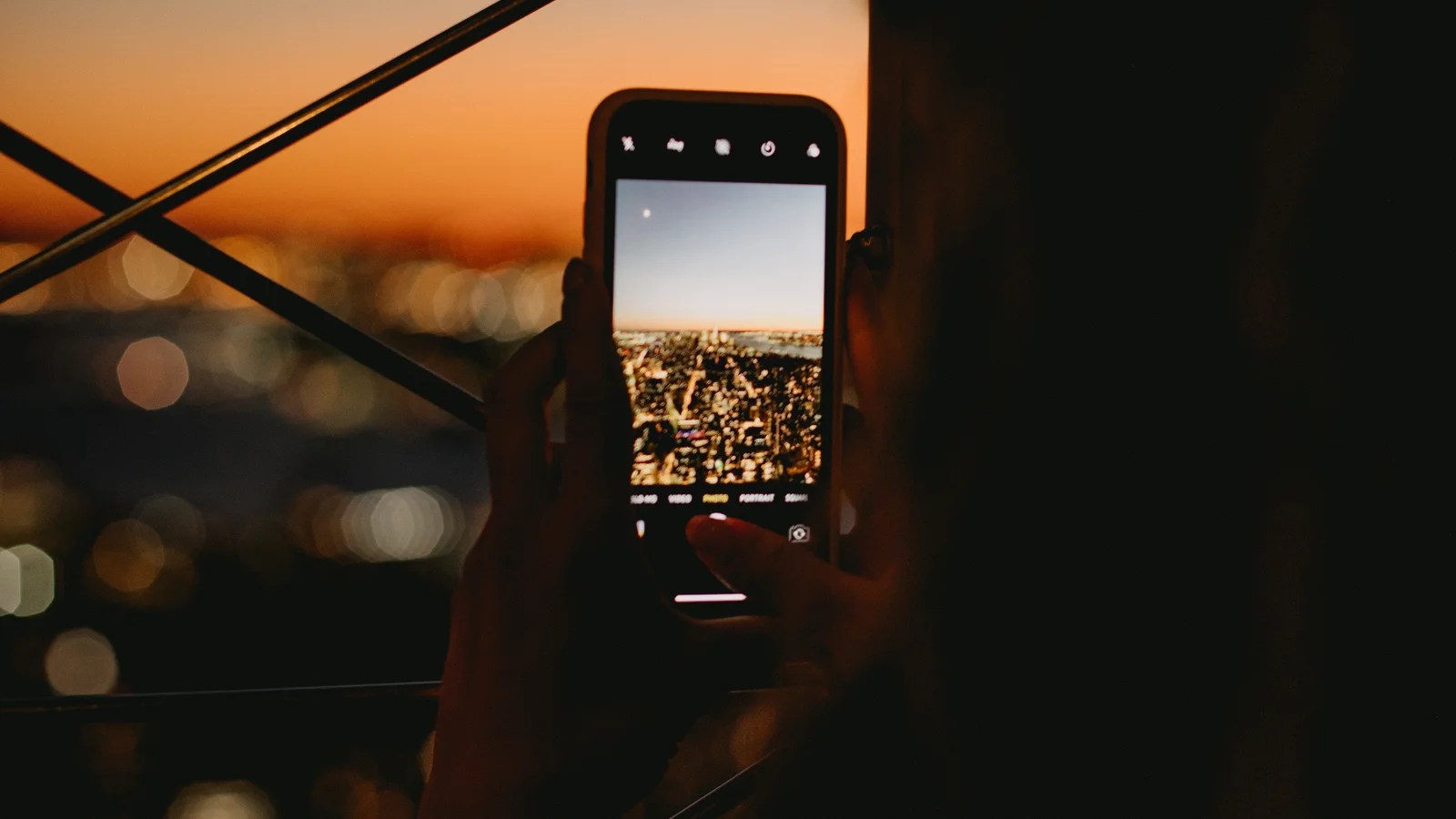 Človek fotografuje osvetlené mesto mobilom za súmraku