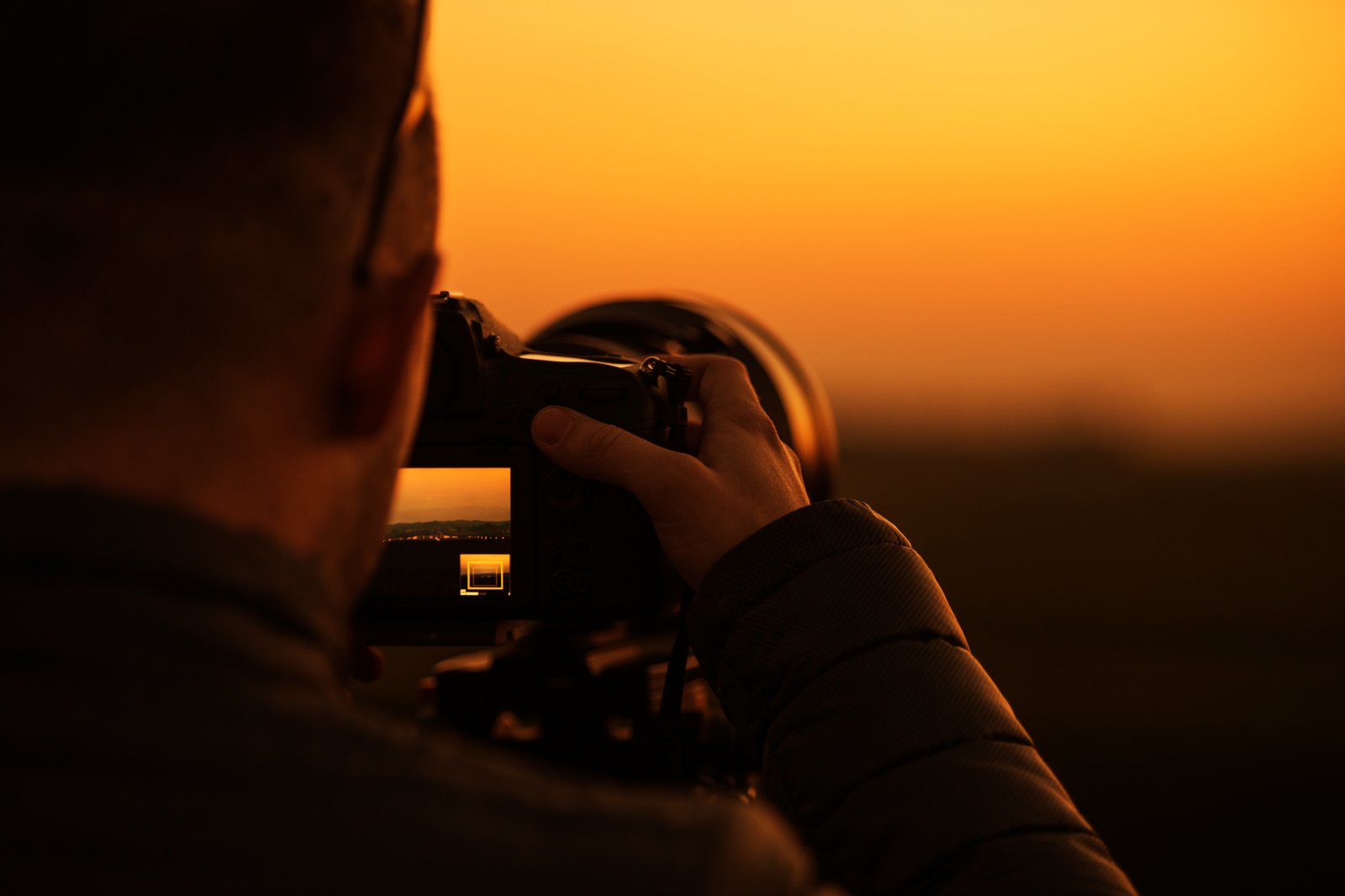 Fotograf s digitálnym fotoaparátom zachytáva západ slnka nad krajinou