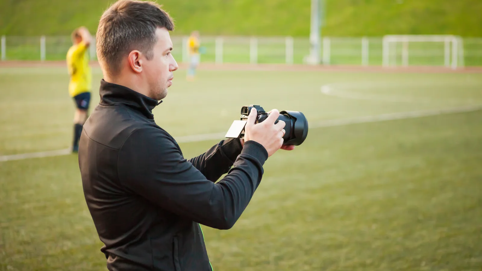 Fotograf s fotoaparátom pri športovom ihrisku