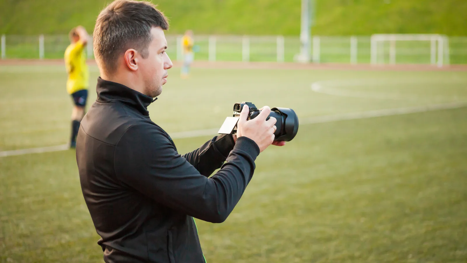 Fotograf s fotoaparátom pri športovom ihrisku