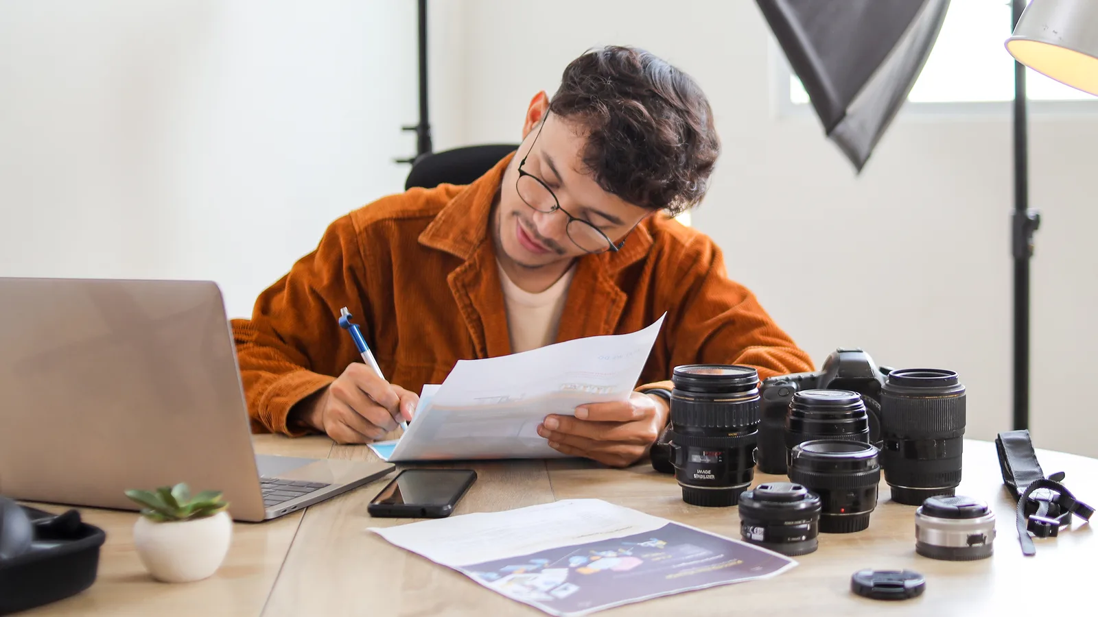 Fotograf kontroluje dokumenty pri pracovnom stole s fotoaparátmi