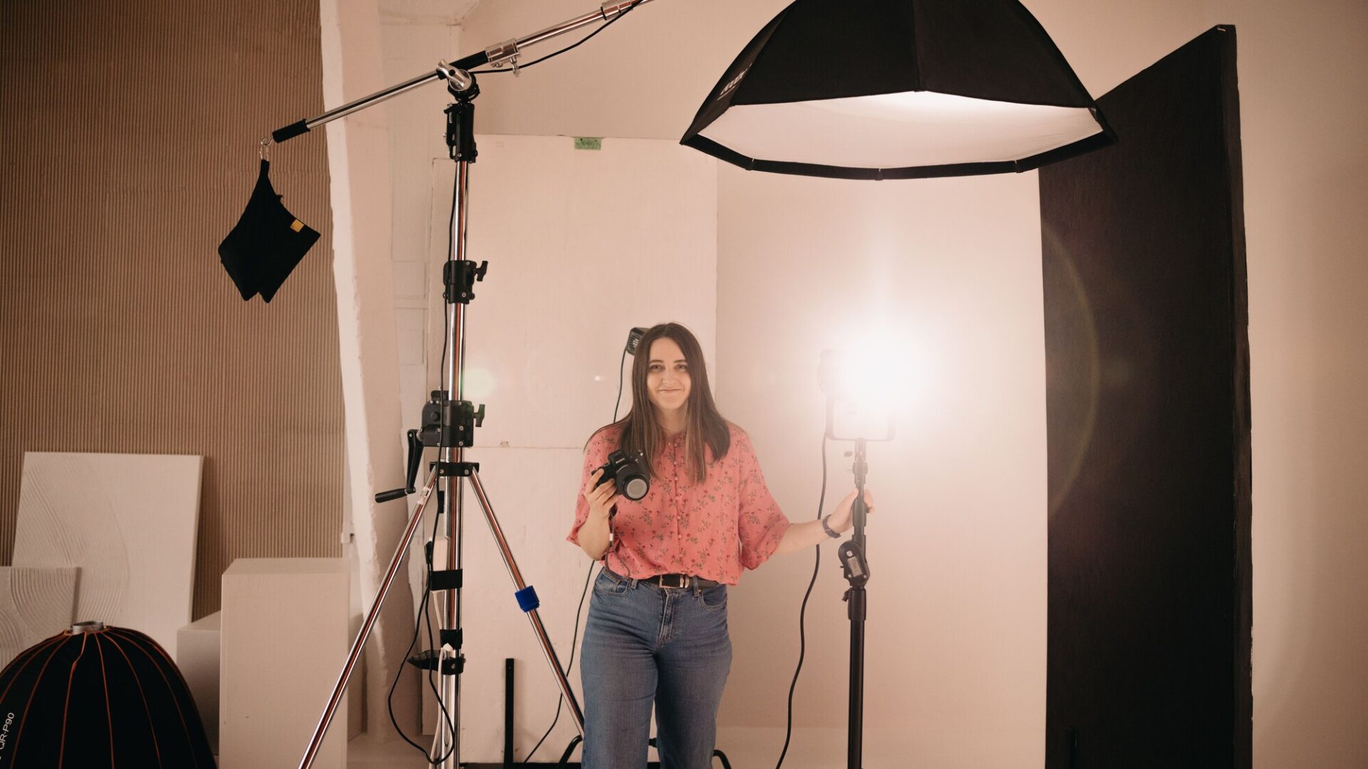 Fotografka s fotoaparátom a osvetlením v ateliéri pred svetlým pozadím