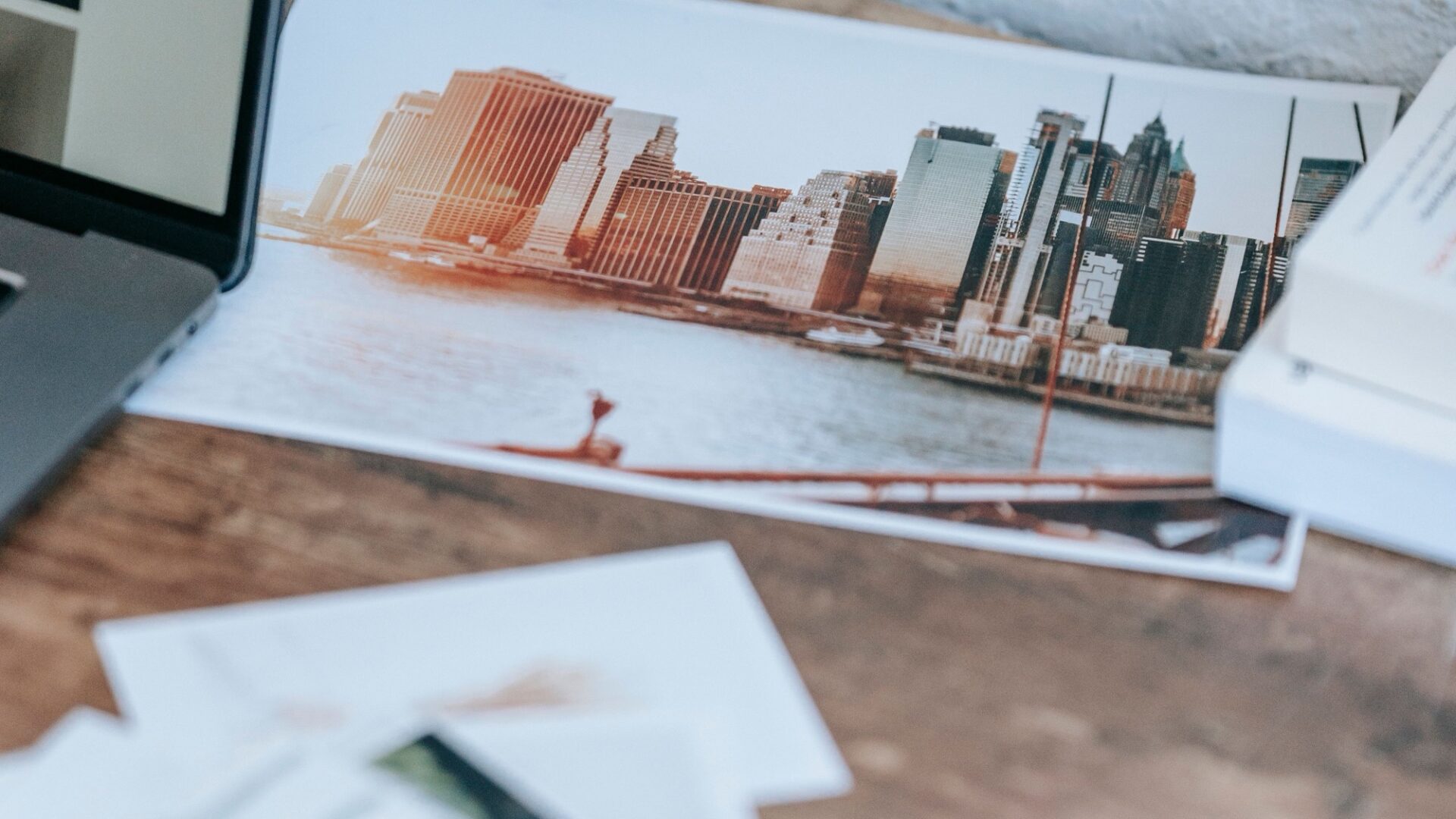 Vytlačené mestské fotografie na pracovnom stole vedľa notebooku