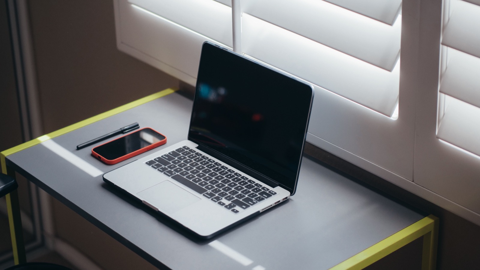Notebook a smartfón na pracovnom stole pri okne